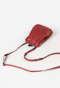 Red leather handbag with a soft texture, a fold-over design, and an adjustable strap. Features black hardware and a sleek, minimalist shape.
