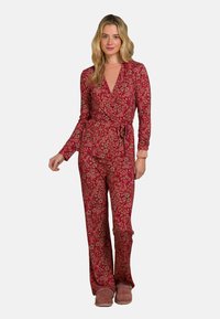 Roter Jumpsuit mit Blumenmuster, langen Ärmeln, Wickeldesign, gebundenem Taillenbund und ausladenden Beinen, kombiniert mit rosa Hausschuhen.