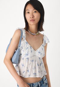 White floral blouse with ruffled shoulders, featuring blue and green flowers. Paired with a light blue denim bag and layered bead necklace.