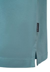 Polo shirt azzurro chiaro con tessuto testurizzato, spacchi laterali e una piccola etichetta nera con il nome del marchio sull'orlo.