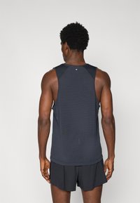 Varrukaideta tumesinine tank-top, valmistatud hingavast kangast, ümmarguse kaelusega ja mugava lõikega, kantud mustade lühikesed pükste abil.