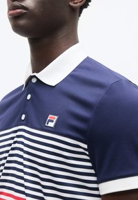 Gros plan sur une personne portant un polo rayé bleu marine et blanc avec un col blanc et un petit logo sur la poitrine.