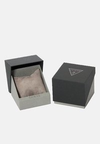 Schwarze und graue zweigeteilte Box mit einer strukturierten Oberfläche. Im Inneren befindet sich ein weiches, graues Stoffkissen. Das Futter trägt das Branding "GUESS".