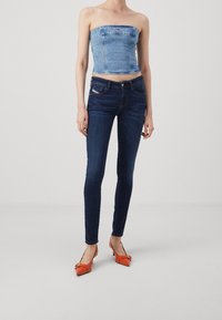 Ljusblå jeans-top utan axelband, kombinerad med mörkblå skinny jeans och orangea högklackade skor med spets och rosett, mot en minimalistisk bakgrund.