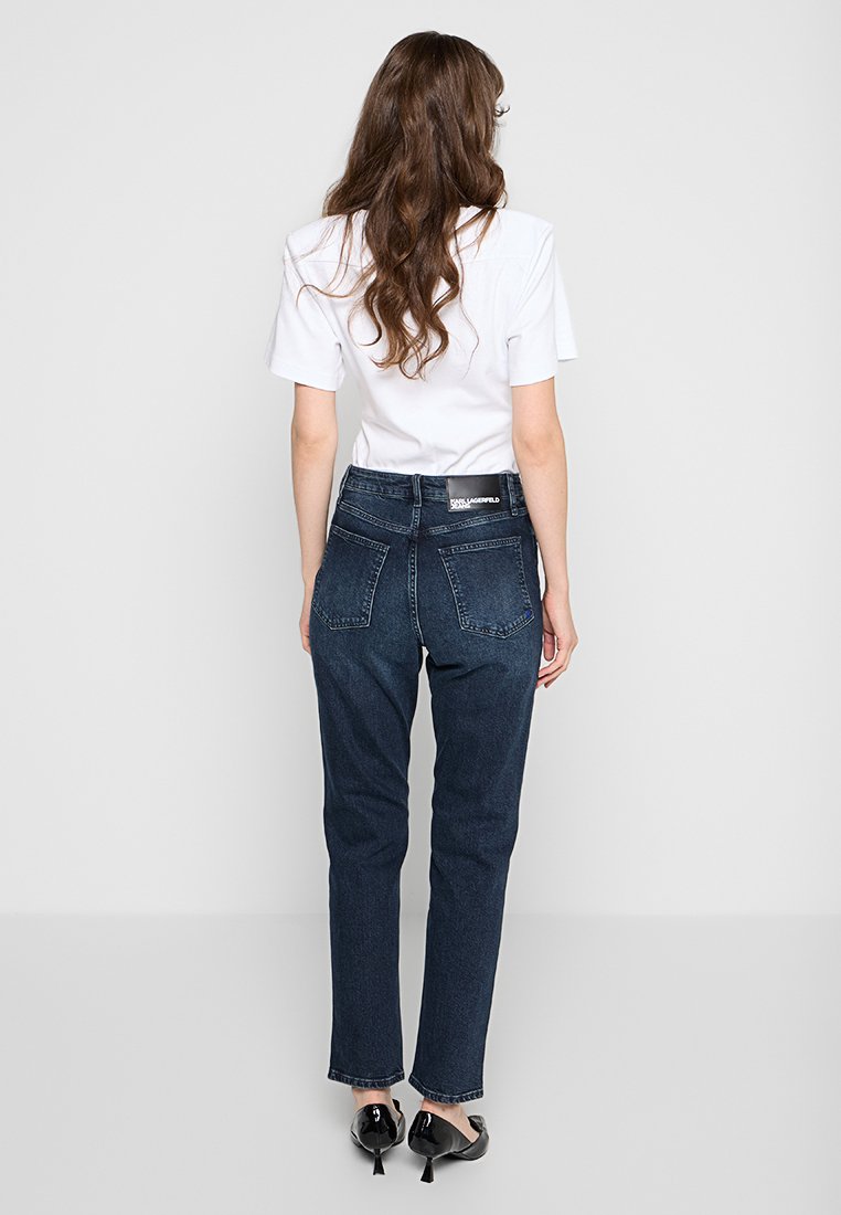 Dunkelblaue Jeans aus Denim, hochtailliert mit geradem Bein, mit Gesäßtaschen und dezentem Markenetikett am Bund. Kombiniert mit einem weißen T-Shirt.