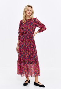 Floral long-sleeve dress with a ruffled neckline and tiered skirt. Features a pink and blue flower pattern on light fabric. Black flat shoes.