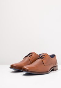 Braune Lederschuhe mit glatter Oberfläche, runder Zehenpartie, niedrigem gestapeltem Absatz und kontrastierenden Schnürsenkeln, verziert mit dezenten Nähdetails.