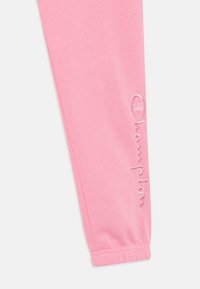 Rozā sporta bikses no mīksta auduma, ar elastīgām malām un izšūtu "Champion" logo pa sānu.