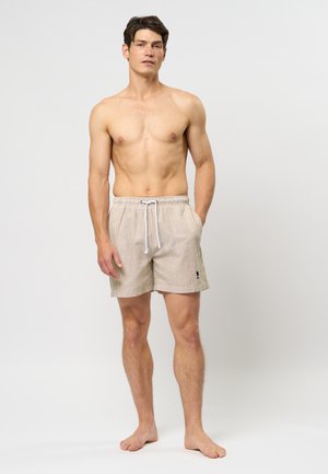 Hellbraune gestreifte Badeshorts mit elastischem Bund und Kordelzug, ausgestattet mit einem kleinen Logo am Bein. Der Stoff wirkt weich und texturiert.