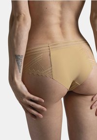 Sous-vêtements en dentelle et tissu beige avec un bord festonné, une texture lisse et un motif en maille géométrique à l'arrière.