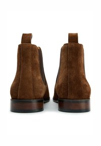 Brown suede ankle boots with elastic side panels, pull tabs, and a stacked wooden heel, featuring a smooth texture and rounded toe design.