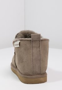 Brune semsket ankelstøvel med myk pelsforing, sømdetaljer og flat gummisåle. Bakpå har den et merketikett og en løkke.