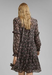 Vestido negro de flores con mangas largas, acentos de volantes y falda en capas. Presenta un patrón floral colorido sobre tela transparente.