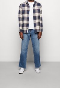 Camicia a quadri navy e crema, design con bottoni, con taschino sul petto. Abbinata a jeans a gamba larga azzurri e sneakers bianche.