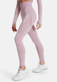 Vaaleanpunaiset korkeavyötäröiset leggingsit, joissa on ribbitekstuuri ja sivupaneeli. Varustettu valkoisella "SQUATPROOF" logolla. Yhdistetty valkoisiin urheilukenkihin.