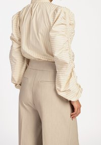 Blouse à rayures crème avec des manches bouffantes et une taille cintrée, associée à un pantalon taille haute beige clair avec des poches latérales.