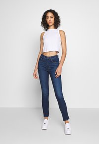Top corto blanco combinado con jeans ajustados de color azul oscuro y zapatillas blancas. Tejido suave con un diseño entallado que acentúa la silueta.
