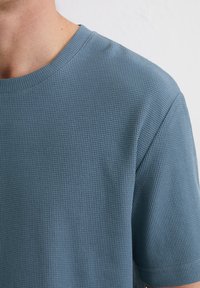 T-shirt met wafelstructuur in het blauw, met een ronde hals en korte mouwen. De stof toont een rasterachtig patroon.