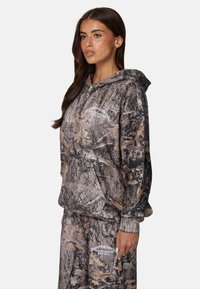 Sweat à capuche et pantalon au motif camouflage présentant des nuances de marron et de beige. Fabriqué en tissu doux avec une coupe décontractée. Détail logo blanc.
