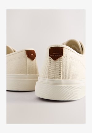 Leinenschuhe in Creme mit strukturierter Oberfläche, mit braunen Lederakzenten an der Ferse und einer Gummisohle.