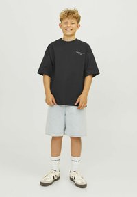Svart bomulls-t-shirt med korta ärmar, kombinerad med ljusblå denimshorts. Accessoarer inkluderar vita strumpor och beige sneakers med svarta detaljer.