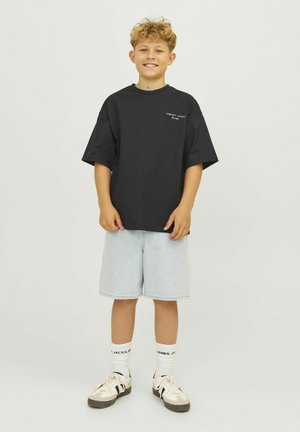 Camiseta de algodón negra con mangas cortas, combinada con pantalones cortos de mezclilla azul claro. Los accesorios incluyen calcetines blancos y zapatillas beige con acentos negros.