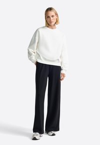 Sudadera blanca de corte relajado, combinada con pantalones anchos negros. Tejido suave con puños y cinturilla acanalados. Un calzado ligero completa el look.