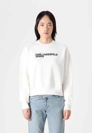 Sweatshirt en coton blanc avec un col rond, arborant le texte noir "KARL LAGERFELD JEANS" à l'avant. Coupe surdimensionnée avec des poignets côtelés.