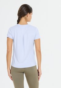 Lichtblauw shirt met korte mouwen van gladde stof, met een centrale plooi aan de achterkant en een ronde halslijn. Gepaard met aansluitende olijfgroene leggings.