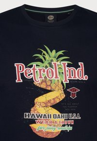 Námořnická modrá bavlněná tričko s velkým grafickým vzorem ananasu, textem "Petrol Ind." v bílé a červené barvě a sloganem pod ním v barevném písmu.