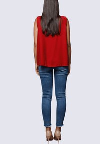 Top rojo sin mangas con un corte holgado, combinado con jeans ajustados de mezclilla azul medio y zapatos de tacón nude. Tela ligera de color sólido.