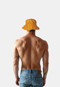 Orange bucket hat med ett lekfullt mönster, bärs av en person med bar rygg, i kombination med blå denimshorts.