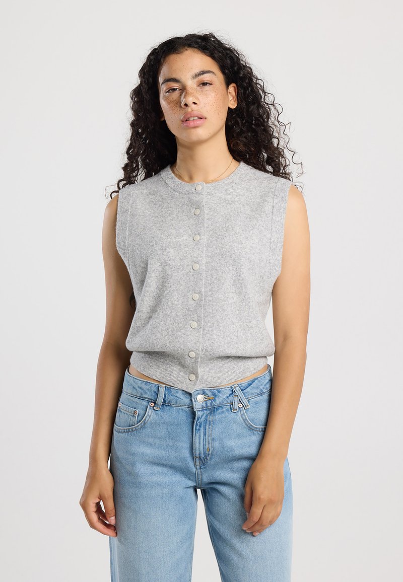 Gray sleeveless knit top with a round neckline and button closure down the front, paired with high-waisted blue jeans. Simple textured fabric.