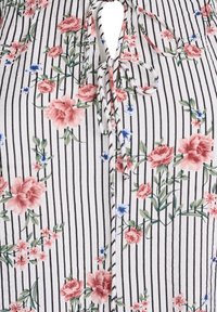 Blouse florale avec des rayures verticales noires et blanches, ornée de roses roses et de fleurs bleues, et un détail de nœud à l'avant. Texture de tissu douce.