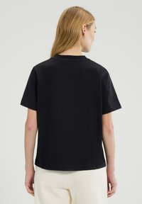 Czarny bawełniany t-shirt z krótkim rękawem i okrągłym dekoltem. Gładka tekstura, luźny krój i wykończony dół w talii.