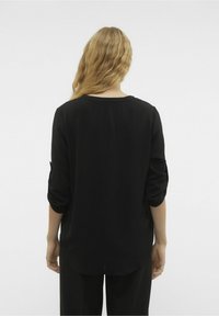 Blusa nera con finitura testurizzata, maniche a tre quarti arrotolate ai polsi e scollatura rotonda, mostrata da dietro.