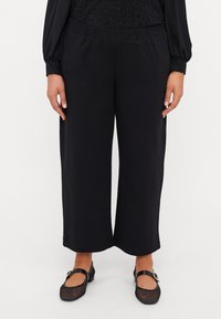 Black wide-leg trousers with a soft fabric, featuring an elastic waistband. Paired with black mesh Mary Jane shoes.