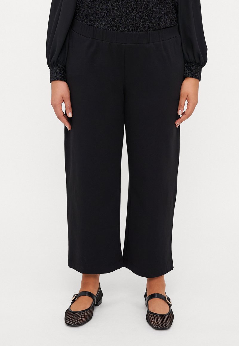 Black wide-leg trousers with a soft fabric, featuring an elastic waistband. Paired with black mesh Mary Jane shoes.