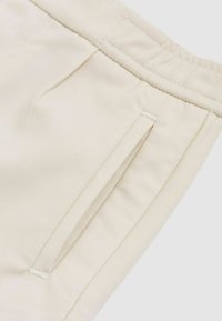 Creamfärgad tyg med en slät textur, som har en sidficka med en enkel design och subtila sömnadsdetaljer vid midjan.