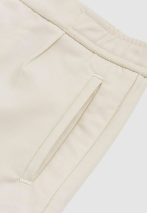 Cremfarbener Stoff mit einer glatten Textur, versehen mit einer Seitentasche mit einem schlichten Design und dezenten Stickdetails am Taillenbund.