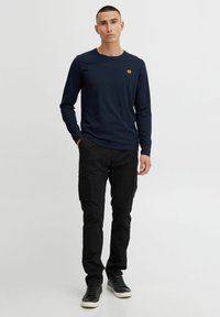 Long-sleeve navy T-shirt with a round neck and a small circular logo, paired with black cargo pants featuring side pockets and zippers.