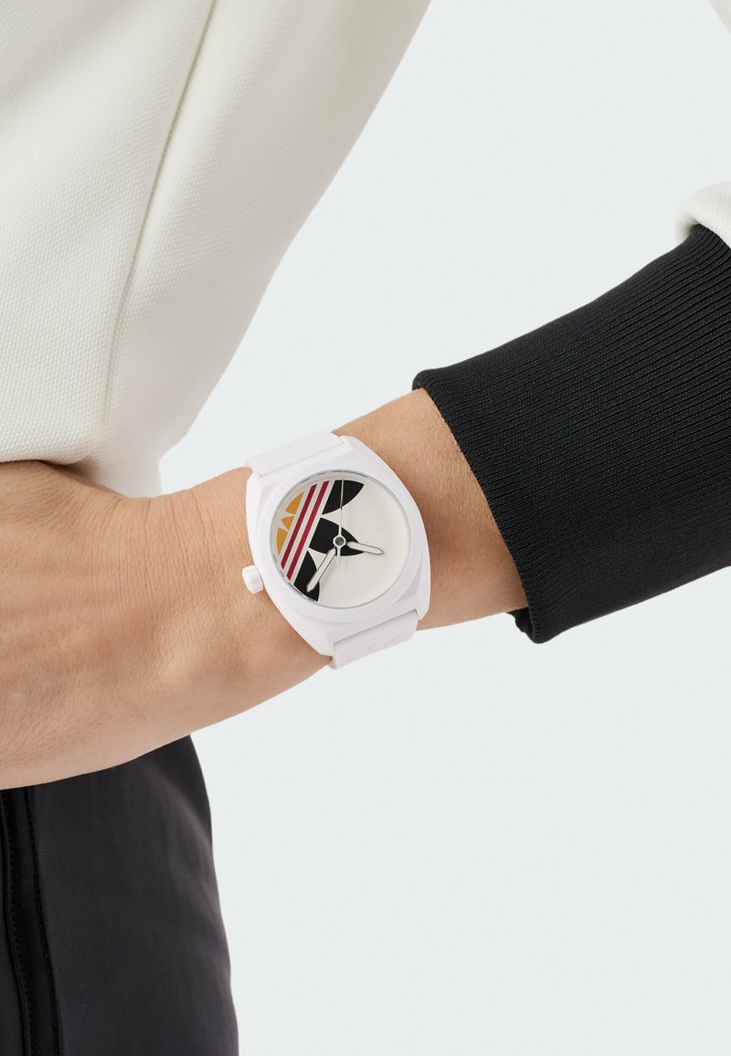 Reloj de silicona blanco con esfera redonda que presenta acentos en negro y naranja, franjas multicolores y manecillas simples de hora y minuto en plata.