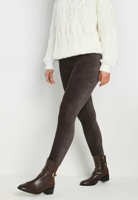 Leggings en velours côtelé marron avec une coupe ajustée, assortis à un pull en tricot torsadé crème et des bottines marron avec un détail de boucle.