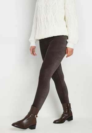 Leggings in cotone color marrone con vestibilità aderente, abbinati a un maglione a maglia a treccia color crema e stivaletti marroni alla caviglia con dettaglio a fibbia.