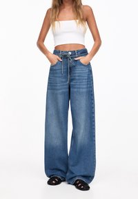 Höga vida jeans i medelblå denim, med dragsko i midjan, sidofickor och en lätt blekt struktur.