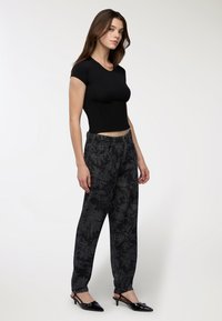 Top aderente nero abbinato a jeans larghi a fantasia scura con design floreale e lunghezza alla caviglia. Le scarpe sono nere lucide con tacco basso.