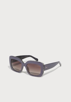 Óculos de sol quadrados com uma armação matte roxa e detalles cinzentos em padrão. Lentes castanhas degradê e uma sensação de robustez. Logotipo da marca na haste.