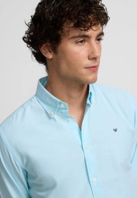 Camisa de botones azul claro en tejido de algodón, con un clásico cuello, un logo sutil en el pecho y botones perlados.