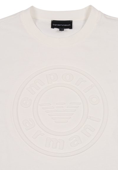 T-shirt bianca in cotone con logo circolare in rilievo che presenta la scritta "emporio armani" e l'emblema dell'aquila al centro. Design con collo rotondo.