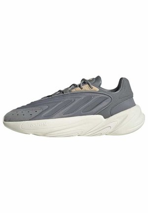 Baskets de sport grises avec accent beige et semelle blanche épaisse et rembourrée, avec des lacets et des trous de ventilation près des orteils.